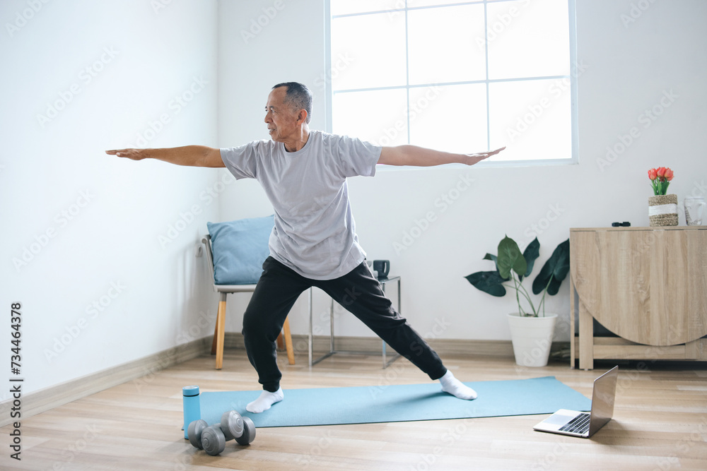 Senior Asian man practicing yoga from laptop on the mat at home