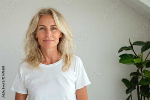 Blonde haired woman in white tshirt in front of white wall with room for artwork photo