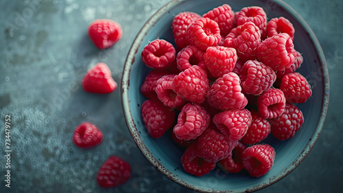 A close-up of juicy, fresh raspberries in a textured blue bowl on a rustic grey background, perfect for a healthy snack. 