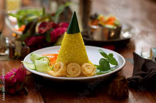Nasi Tumpeng Mini or Nasi Kuning. Yellow rice in a cone shape. A festive Indonesian rice dish with side dishes.