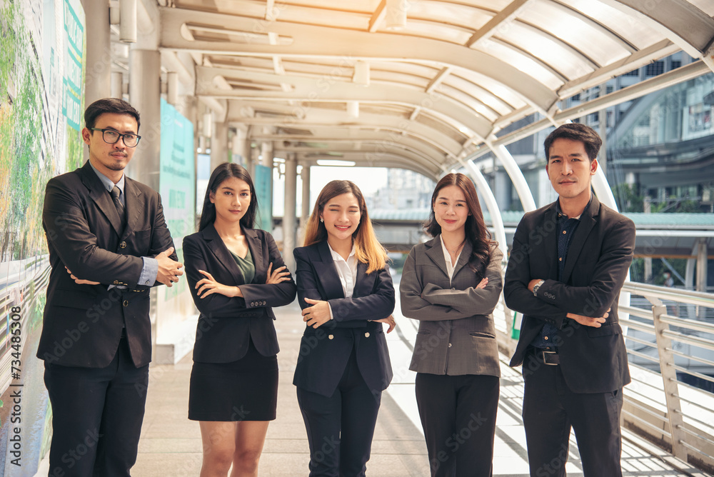 Obraz premium Portrait Group of businesspeople arms crossed smiling look at camera in modern city background. Happy Businessman, businesswoman teams partnership. Business people teams positive teamwork standing.