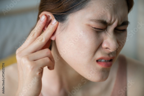Asian woman having an earache problem. An earache is sharp  dull  or burning ear pain in one or both ears.