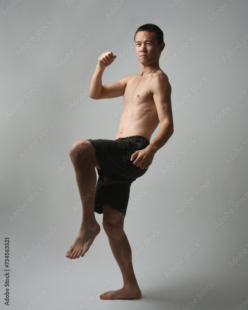 full length portrait of fit asian male model, shirtless with muscles.  gestural ti chi inspired posing with arms reaching out. Isolated on a white studio background with moody silhouette.