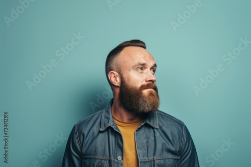 Portrait of a bearded man in a denim jacket on a blue background.
