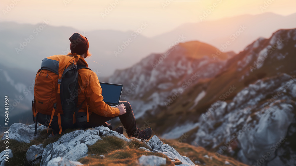 Hiker with laptop seated on mountain summit at sunrise, embracing the remote work lifestyle