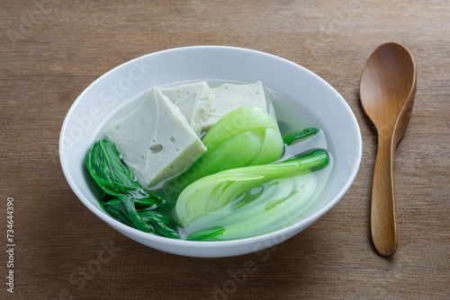 close up view of bok choy soup with bean tofu in a ceramic bowl on wooden table. asian homemade style food concept.