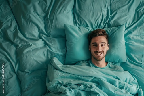 A content man smiles in bed, snuggled under a turquoise blanket with matching pillows, enjoying a peaceful rest.