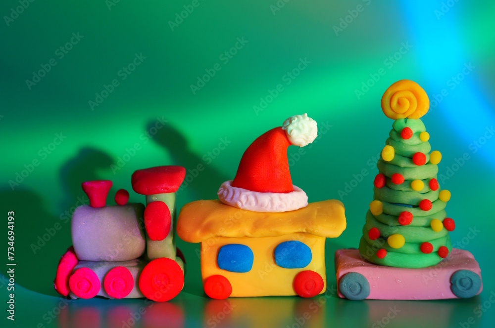Obraz premium A toy train with a Christmas tree and a Santa Claus hat. Christmas decorations. Green background.
