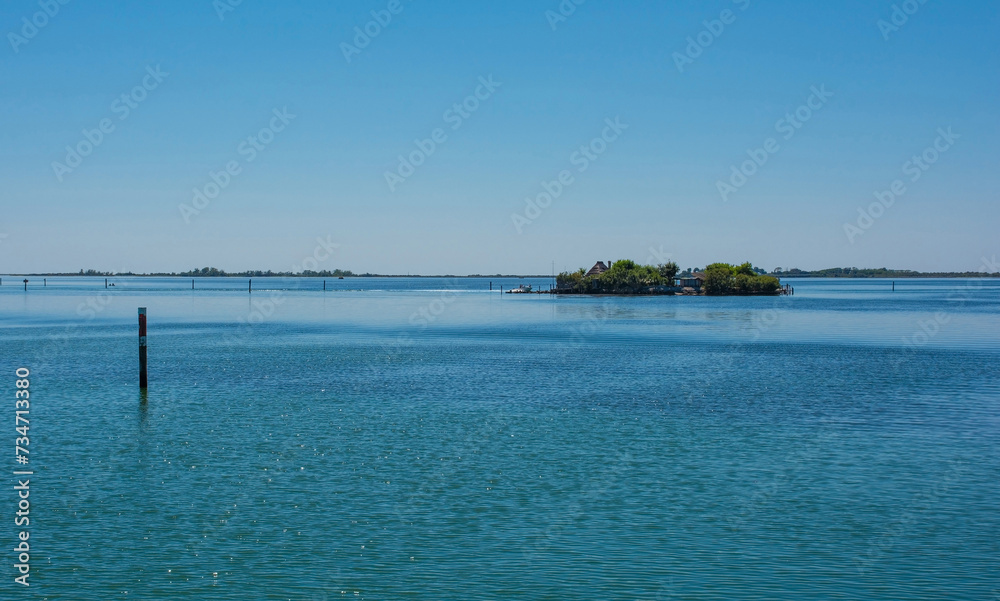 An island in the Grado section of the Marano and Grado Lagoon in Friuli-Venezia Giulia, north east Italy. Channel markers shows the edge of a navigable channel in the shallow waters. August