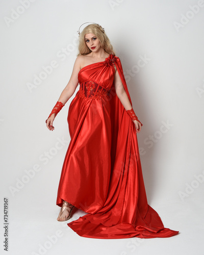 Full length portrait of blonde model dressed as ancient mythological fantasy goddess in flowing red silk toga gown, crown. elegant dancing pose with flowing fabric isolated on white studio background