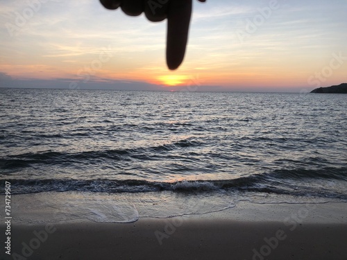 A female hand holding the sun above a sea, Woman hand do peace out with sunset beach background, Holding the day in my finger, Vanilla sky and sunsetting at the end of the day. photo
