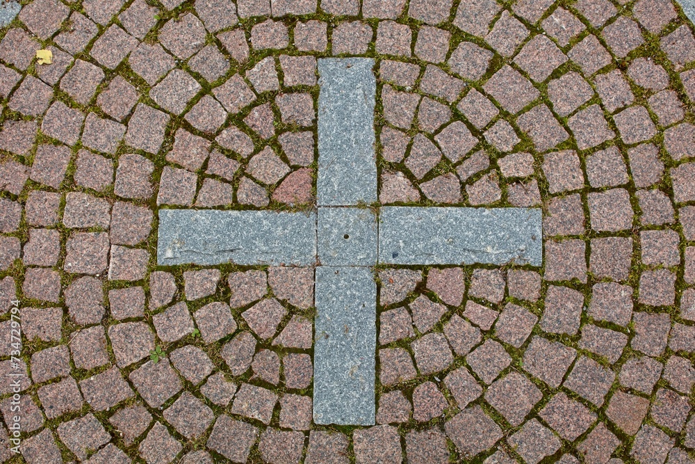 Closeup of cobble stone pavement on ground with a cross.