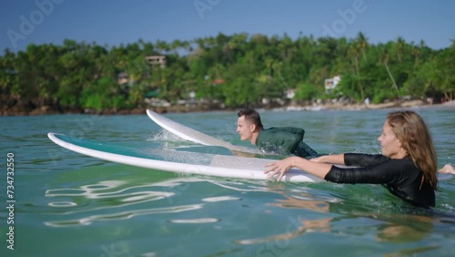 Surfers in swimwear paddling on surfboards. Man, woman in swimsuit swim to lineup lying on board. Couple in love goes to ocean water swells. Family travel recreational activity. Relationship goals.