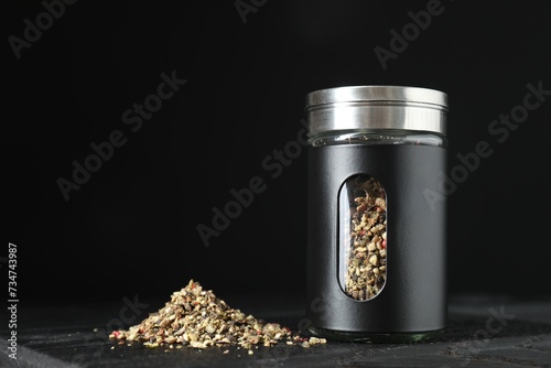 Stylish shaker with pepper on wooden board against black background, closeup. Space for text photo