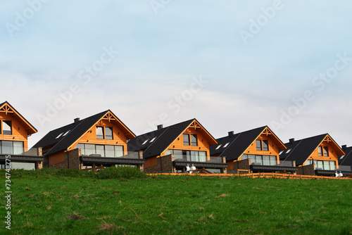 A row of modern wooden houses nestled on a lush green hill under a cloudy sky offering a blend of nature and architecture.