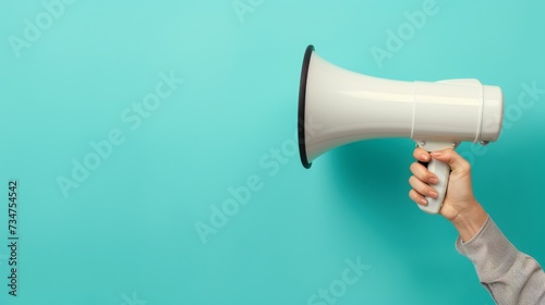 white megaphone held in hand stands out vividly against a plain turquoise background, symbolizing communication and attention