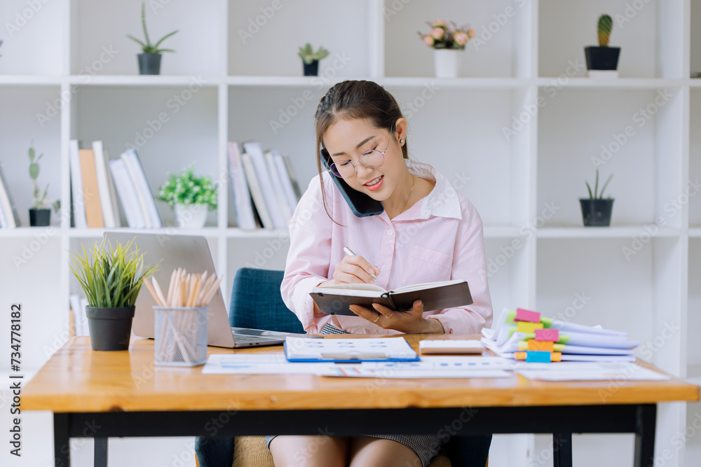 Happy asian young businesswoman using smartphone and laptop at office workplace, Business owner people sme freelance online marketing e-commerce concept. Happy asian young businesswoman using smartphone and laptop at office workplace, Business owner people sme freelance online marketing e-commerce concept.