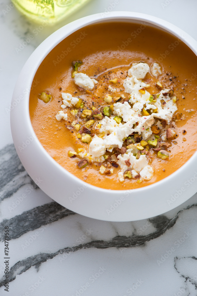 Bowl of sweet potato soup topped with feta cheese and chopped pistachios, vertical shot on a white marble background, elevated view Bowl of sweet potato soup topped with feta cheese and chopped pistachios, vertical shot on a white marble background, elevated view