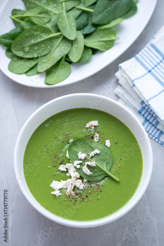 White bowl with spinach cream-soup on a light-grey granite background, vertical shot, elevated view