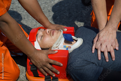 Fotografie A man in head immobilizer tool lying on stretcher long spinal board with safety belt get CPR from rescue team
