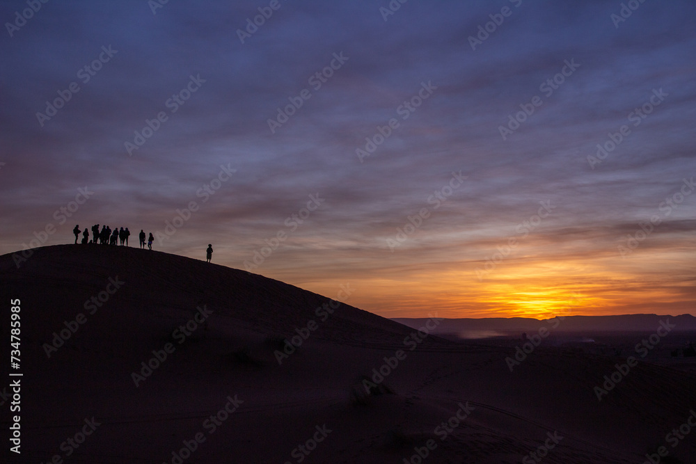 Group of people silhouetted on a dune in a desert landscape at sunrise