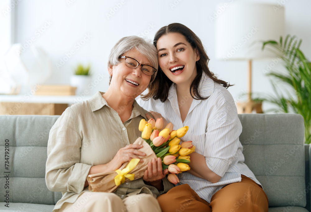 Beautiful young woman and her mother with flowers tulips in hands at home.