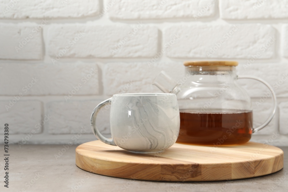 Aromatic tea in glass teapot and cup on gray table against white brick wall, space for text Aromatic tea in glass teapot and cup on gray table against white brick wall, space for text