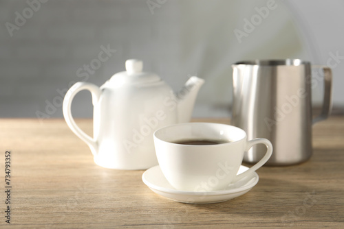 Aromatic tea in cup, teapot and pitcher on wooden table