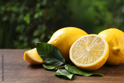 Fresh lemons and green leaves on wooden table outdoors, closeup