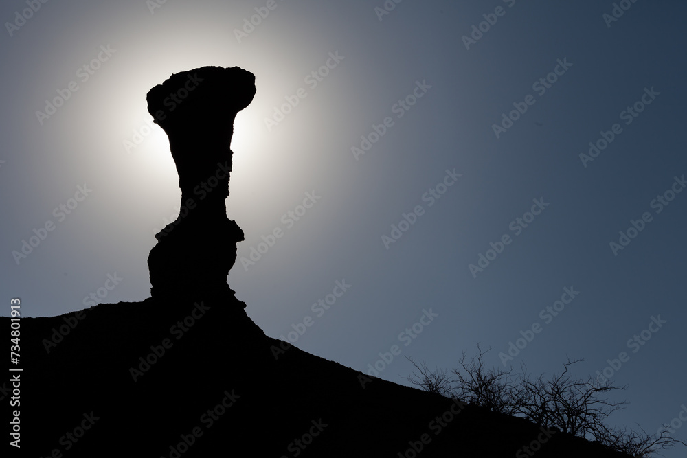 Backlit silhouette of a geological formation against the background of a blue sky. This geological formation blocks the sun and creates a halo of glare that produces a black silhouette.