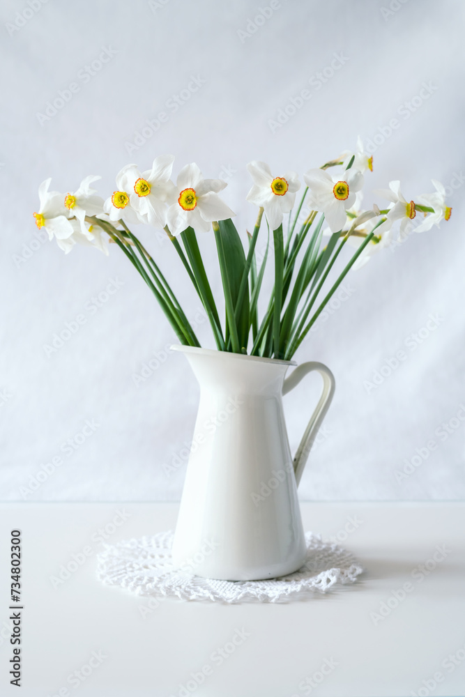 Still life with a blooming bouquet of white daffodils in a white vase on a textured white background.