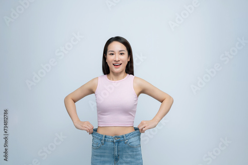 Young smiling happy woman show loose pants on waist after weightloss isolated on white background. © makistock