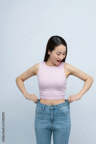 Successful weight loss, asian woman with too large jeans after effective diet, white background