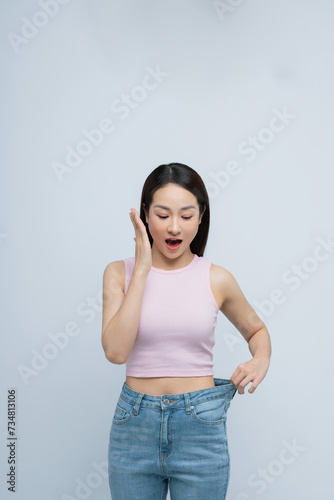 Young smiling happy woman show loose pants on waist after weightloss isolated on white background.