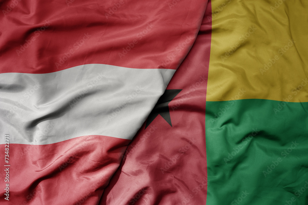 big waving national colorful flag of guinea bissau and national flag of austria .