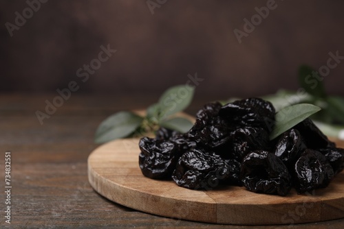 Tasty dried prunes and green leaf on wooden table, closeup. Space for text