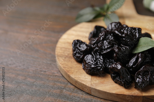 Tasty dried prunes and green leaf on wooden table, closeup. Space for text