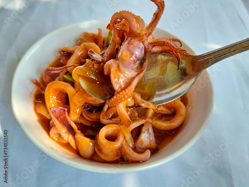 Seafood deliciouse - Cumi Asam Manis or Sweet and Sour Saute Squid with green pete served on white bowl above the Table. Selective focus.
 photo