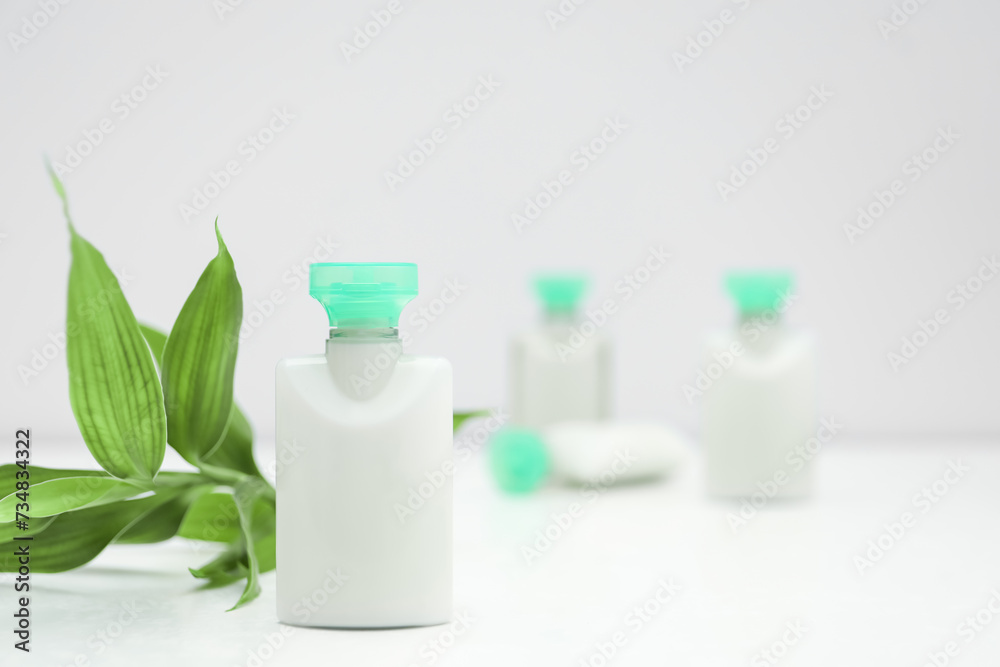 Mini bottle of cosmetic product and green branch on light background. Space for text Mini bottle of cosmetic product and green branch on light background. Space for text