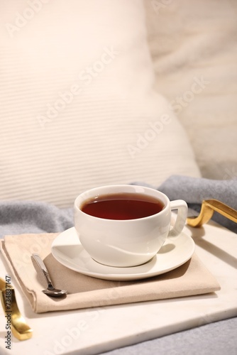 Aromatic tea in cup, saucer and spoon on bed
