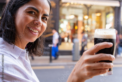 Latin woman looking towards the camera with a Guinness toasting with her companion while enjoying a beautiful autumn morning on her visit to the city of Dublin