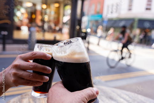 Close-up of two hands toasting each other with Guinness beers on a central Dublin street having a good time on a beautiful autumn morning photo