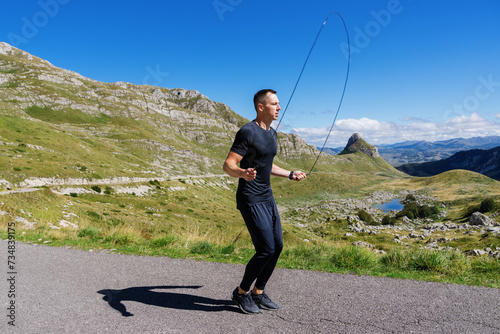 A man trains in a mountainous area. An athlete jumps on a rope.