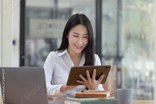 Happy asian young businesswoman using digital tablet  sitting in office working space.