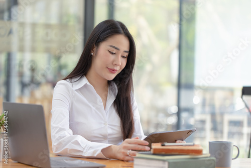 Happy asian young businesswoman using digital tablet sitting in office working space.