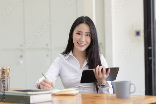 Happy asian young businesswoman using digital tablet  sitting in office working space.