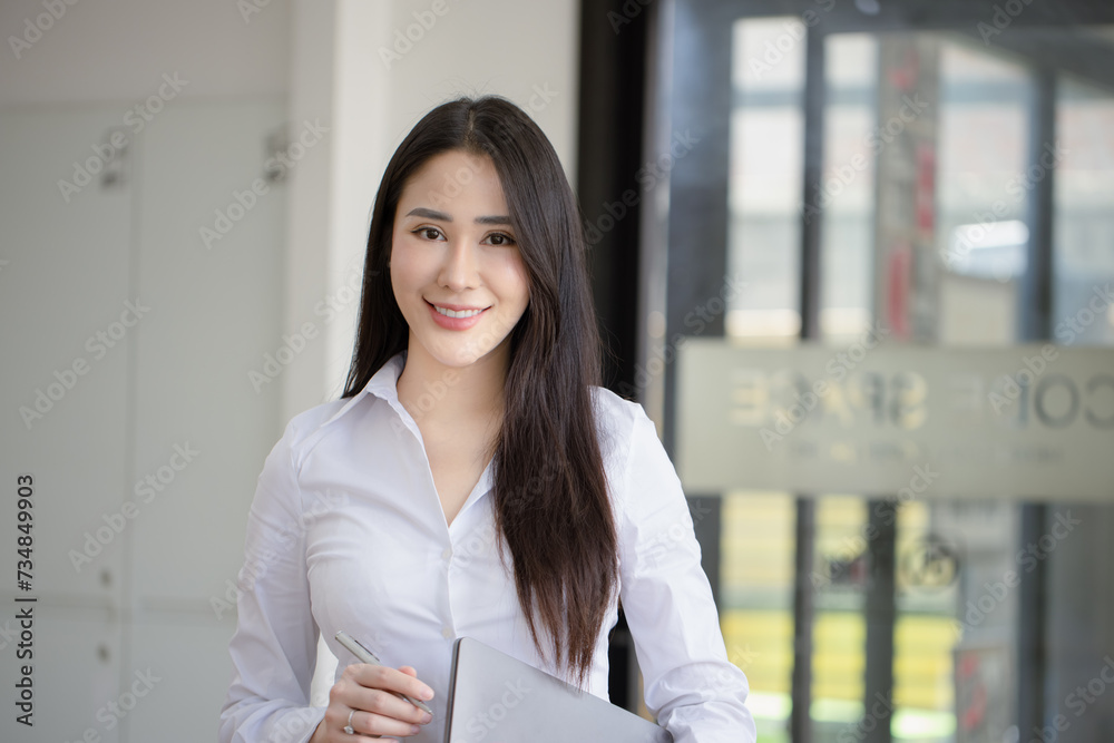 Happy asian young businesswoman holding documents folders in office working space, Asian female employee using laptop talking on the phone at workplace. Happy asian young businesswoman holding documents folders in office working space, Asian female employee using laptop talking on the phone at workplace.