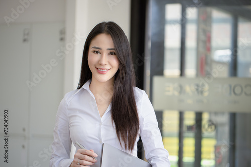 Happy asian young businesswoman holding documents folders in office working space, Asian female employee using laptop talking on the phone at workplace.