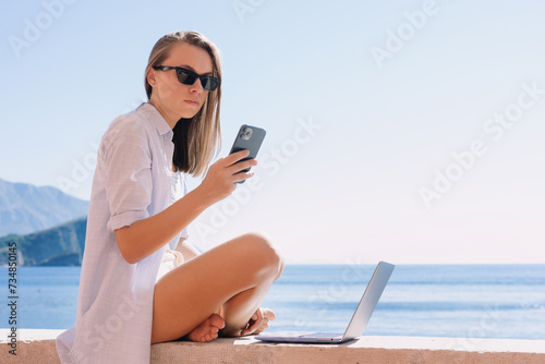 Work during rest. A young woman is sitting on the background of the sea with a laptop. Ability to work from anywhere