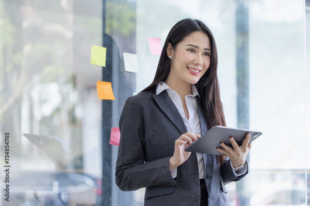 Fototapeta premium Happy asian young businesswoman using digital tablet standing in office office working space.